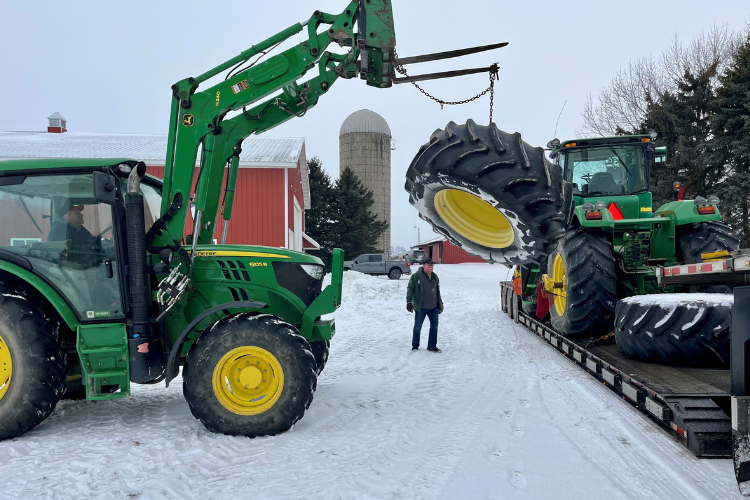 Image of the tractor donated by Duane Stuever's being lifted onto the bed of a truck. 